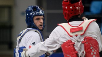 Two male taekwondo athletes look at each other while mid combat in a match