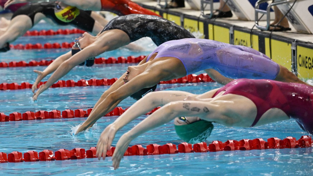 Several female swimmers dive into the pool to start a backstroke race