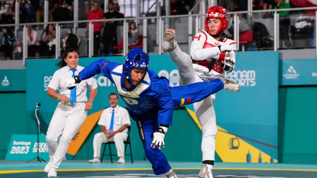 A taekwondo athlete in white and red kicks at an opponent in blue