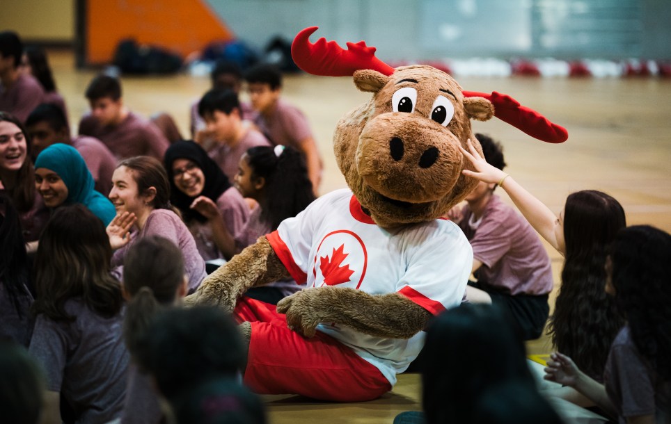 Children gathered at gym with Komak the Moose (mascot).