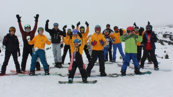 Liam Gill and a group of young Indigenous snowboarders pose on top of a mountain