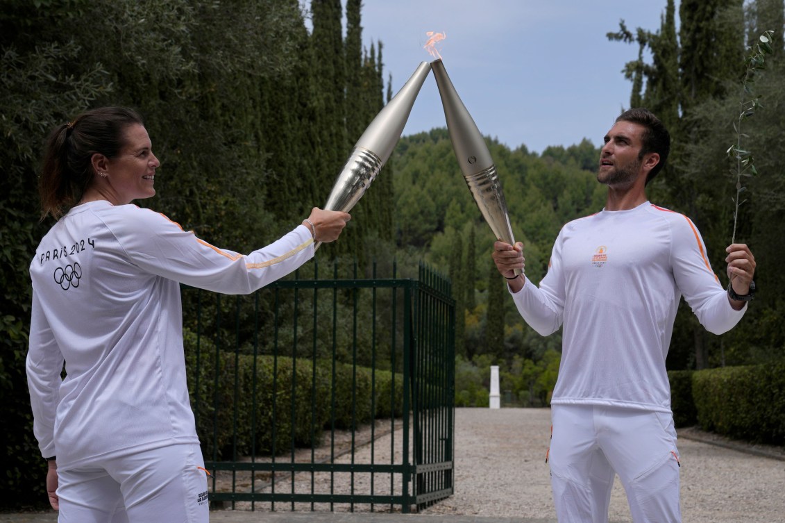Two athletes in white shirts and pants hold their torches together to pass the flame 