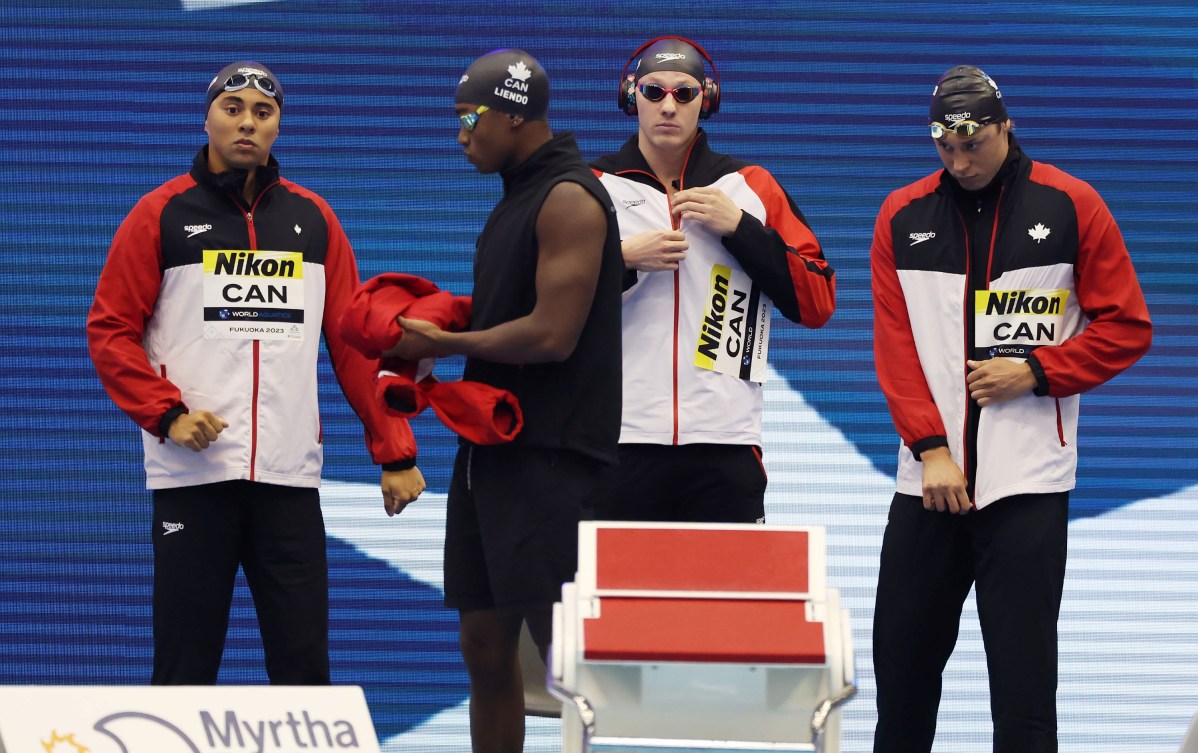 Four Canadian male swimmers on the pool deck in their track suits 