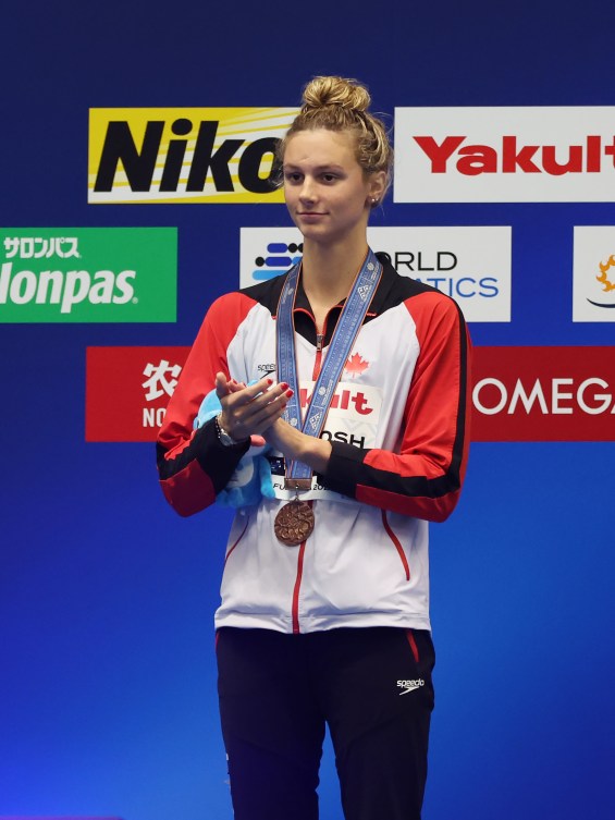 Summer McIntosh applauds while wearing a bronze medal on the podium 