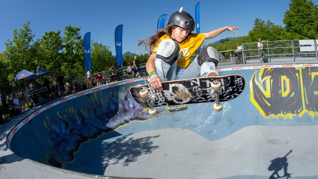 A young female skateboarder flies in the air in a concrete skatepark