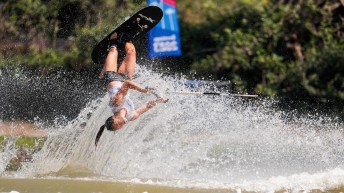 A water skier flies upside down through the wake of a boat in the water