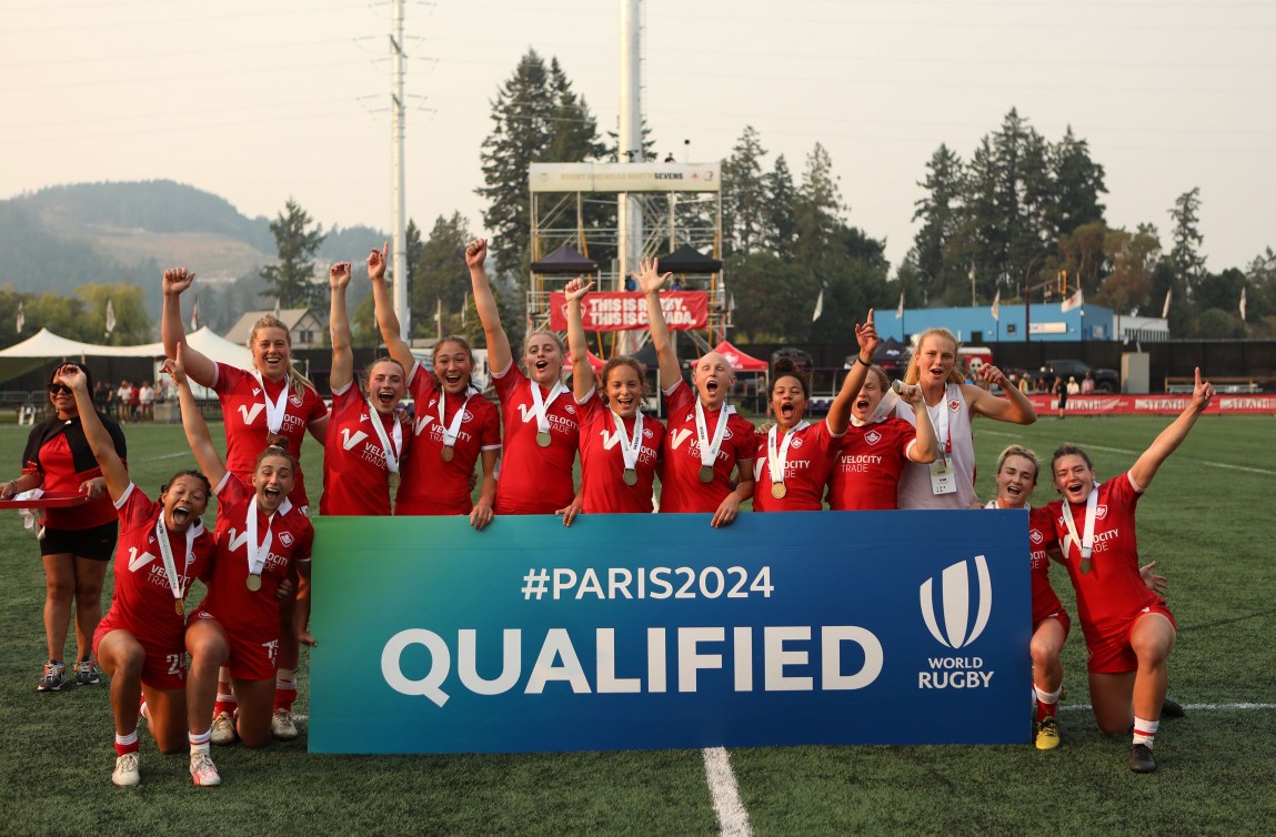 Canadian women's rugby team celebrates behind a big banner that says Paris 2024 qualified