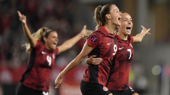 Three Canadian soccer players hold their arms out and scream in joy
