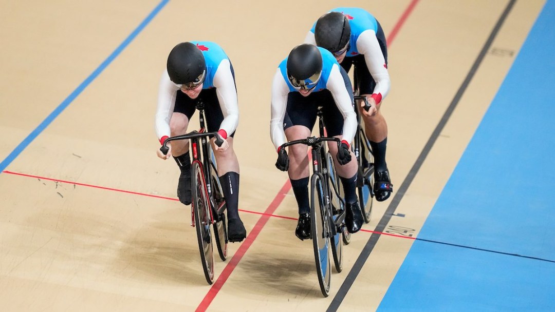 Three female track cyclists in blue jerseys form a line on the velodrome track