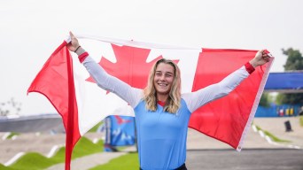 Molly Simpson stands on a BMX track and hoists the Canadian flag overhead.