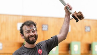 Tugrul Ozer holds his pistol in the air while smiling