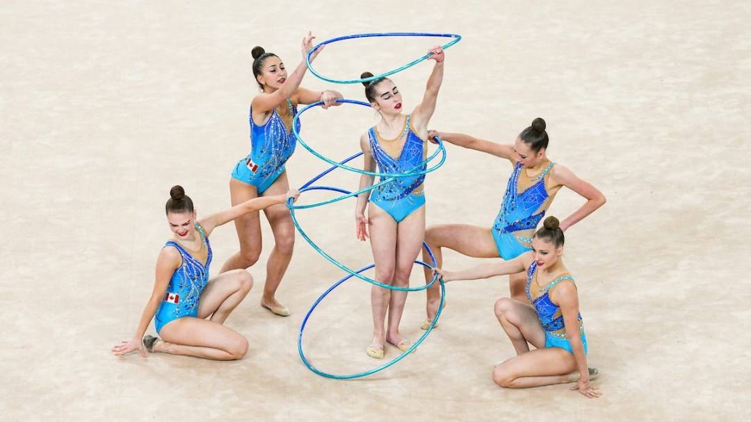 A group of rhythmic gymnasts poses with hoops