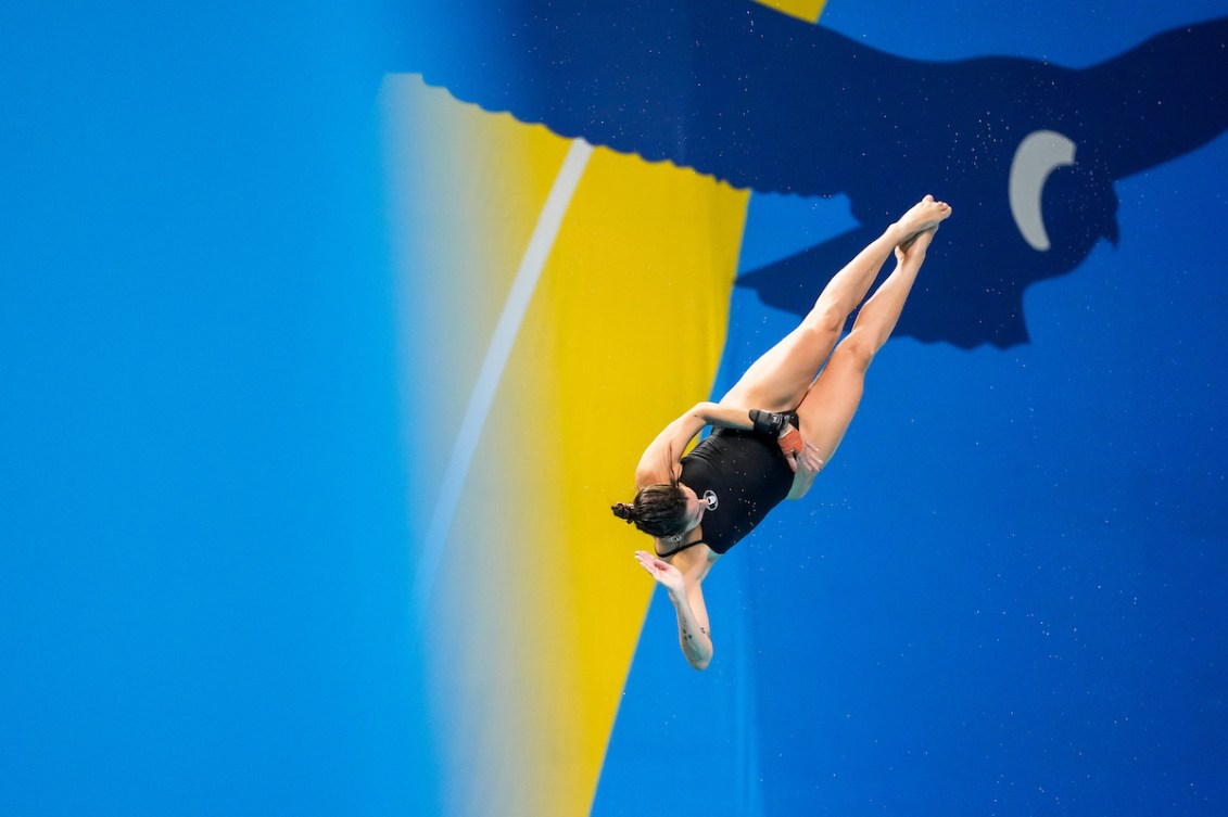 Pamela Ware performs an inverted twist mid air in front of a blue and yellow backdrop