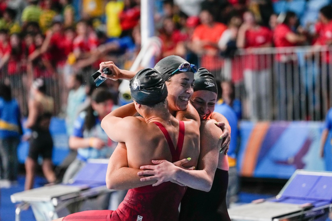 Three swimmers hug each other on the pool deck