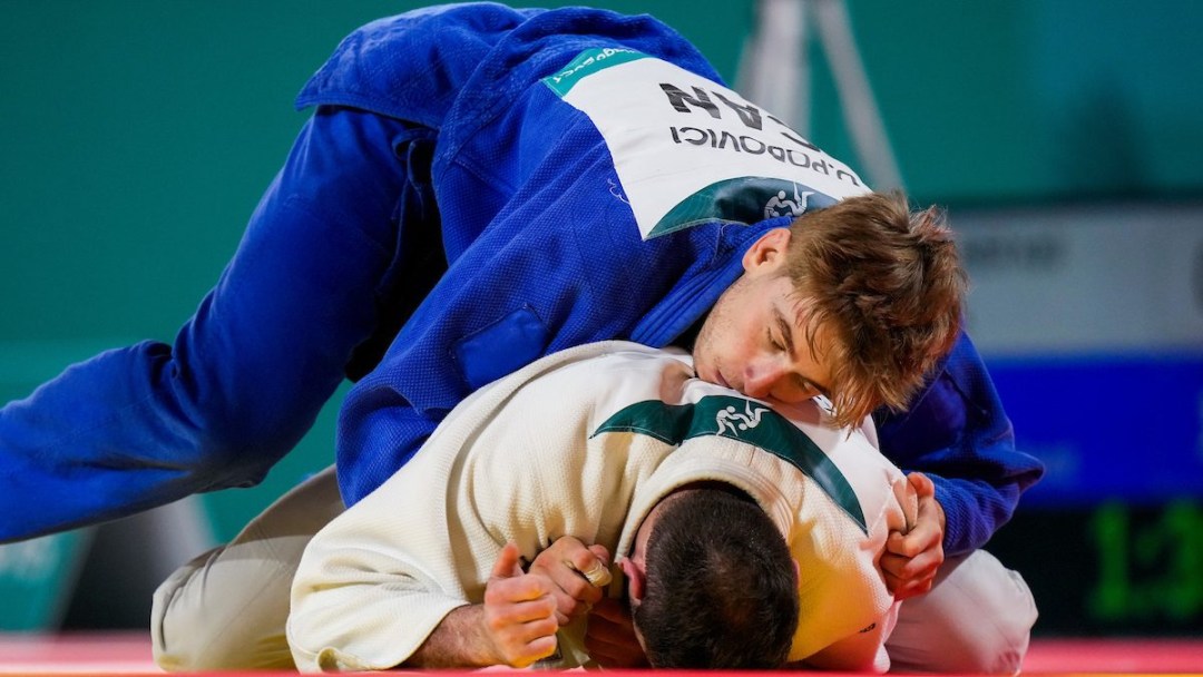 A judoka in blue lies on top of a judoka in white