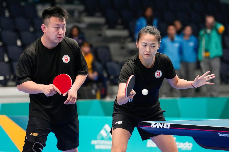 Mo Zhang prepares to hit the table tennis ball while teammate Eugene Wang watches from behind