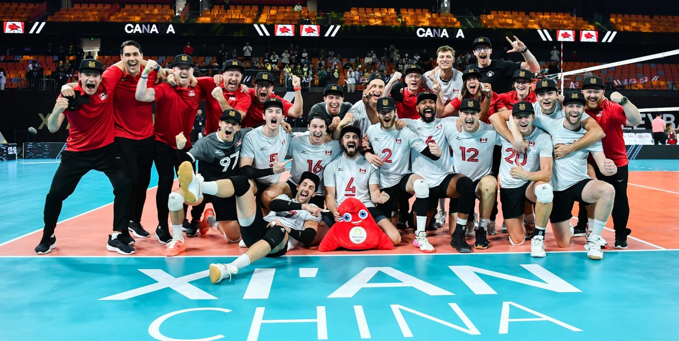 The Canadian men's volleyball team poses on the court with the Paris 2024 mascot