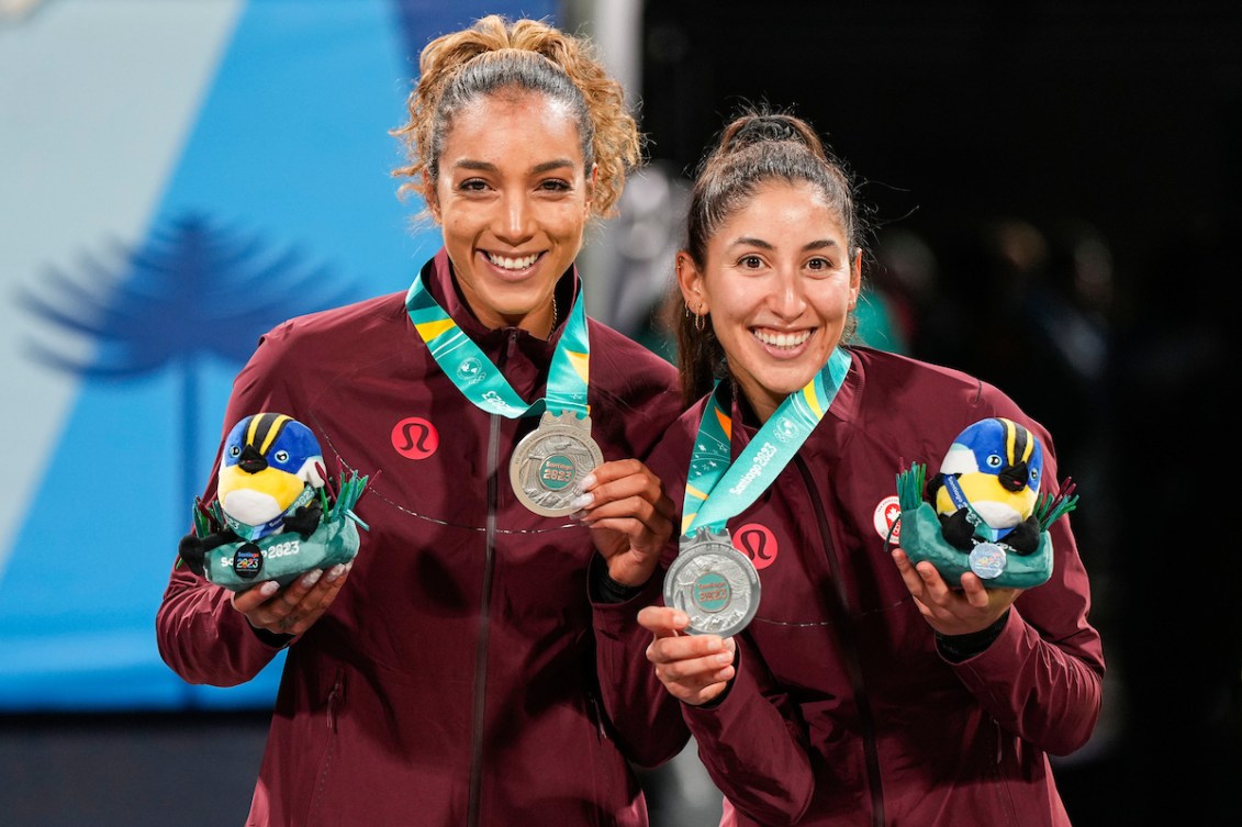 Two athletes in burgundy jackets wear silver medals around their necks and smile