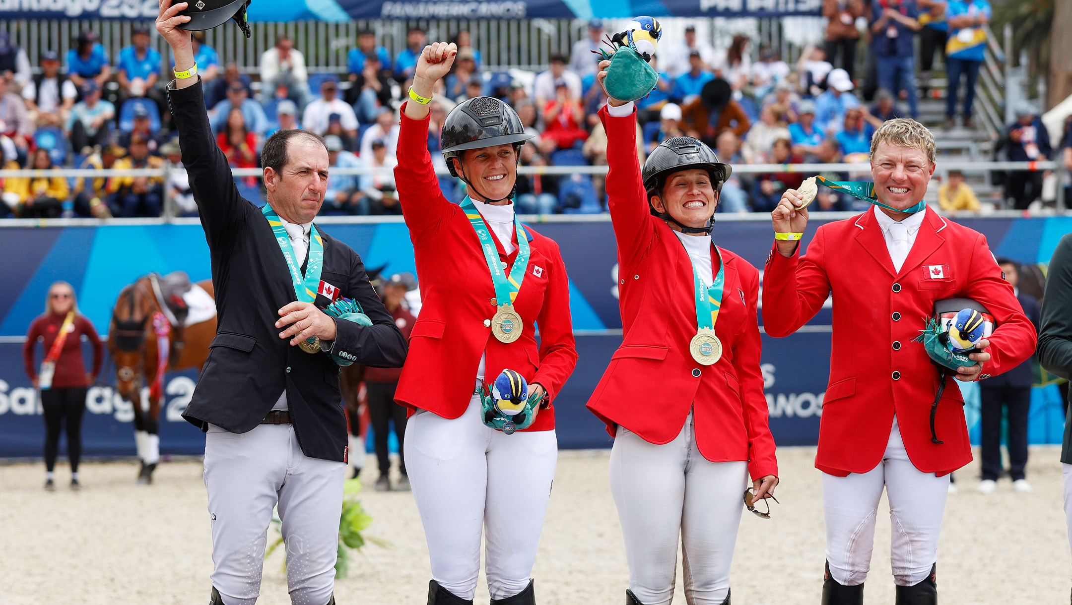 Four horseback riders in Team Canada red and black jacketes and white pants wave to a crowd.