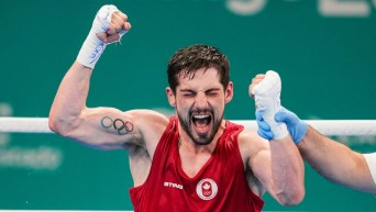 A boxer in red top with an Olympic rings tattoo on his arm screams and pumps his fist in happy reaction