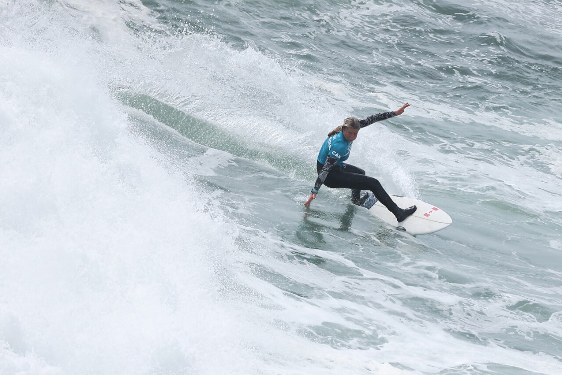 A surfer in a teal top rides a wave