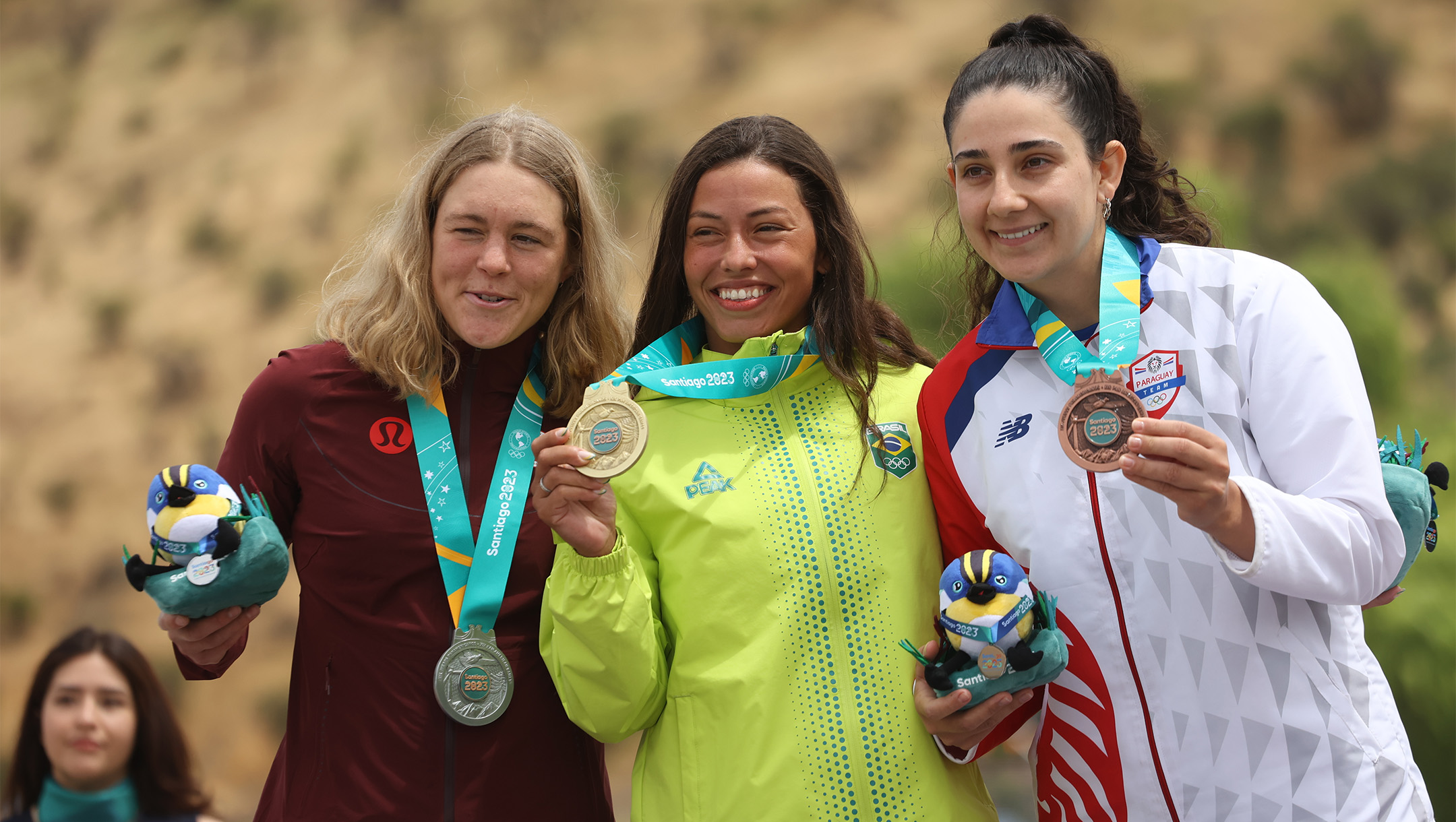 Three female athletes, including one in Team Canada attire stand on the podium.