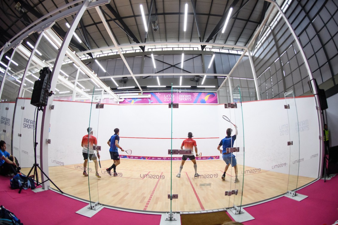 Wide shot of two doubles teams playing on a squash court 