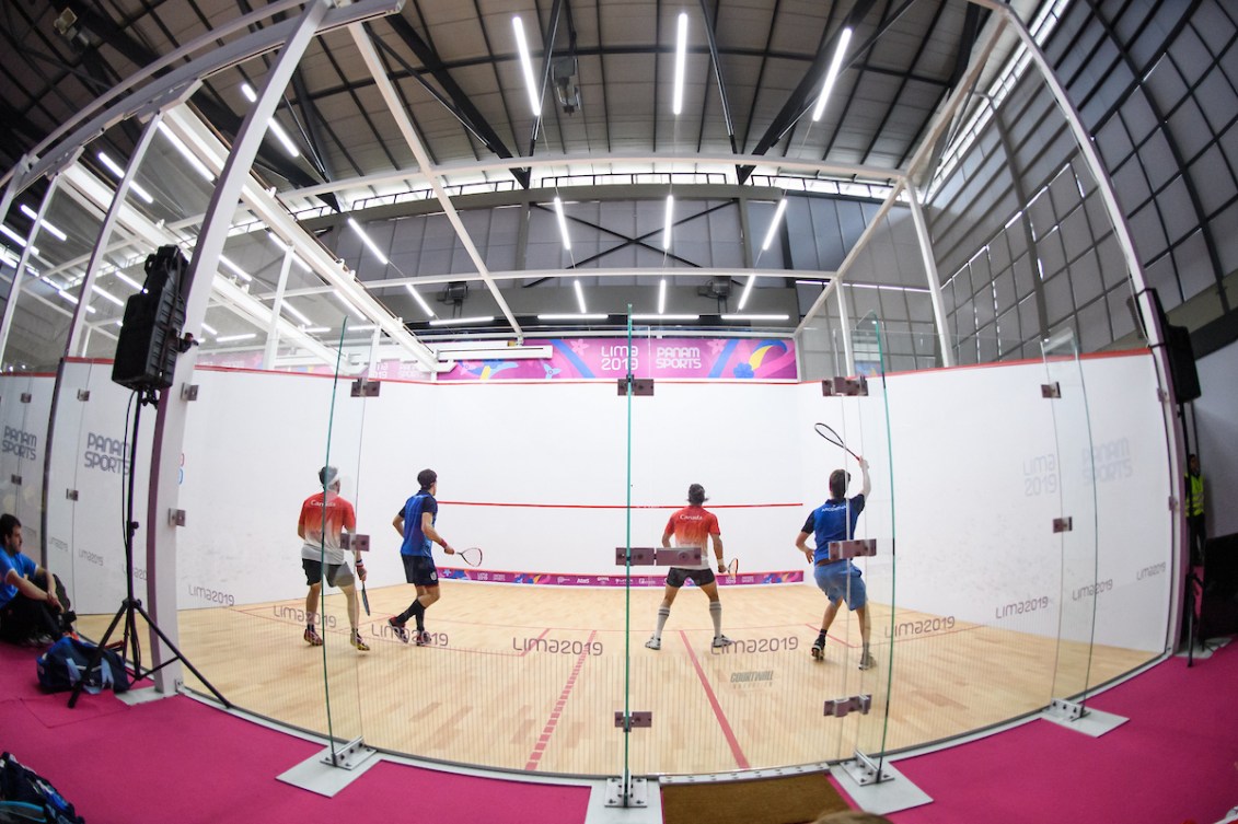 Wide shot of two doubles teams playing on a squash court