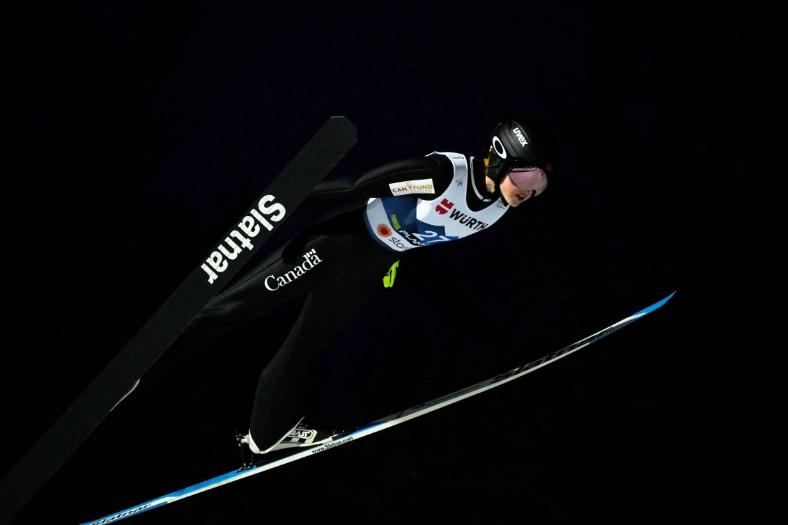Alexandria Loutitt mid ski jump with her skis in a V shape against a black night sky