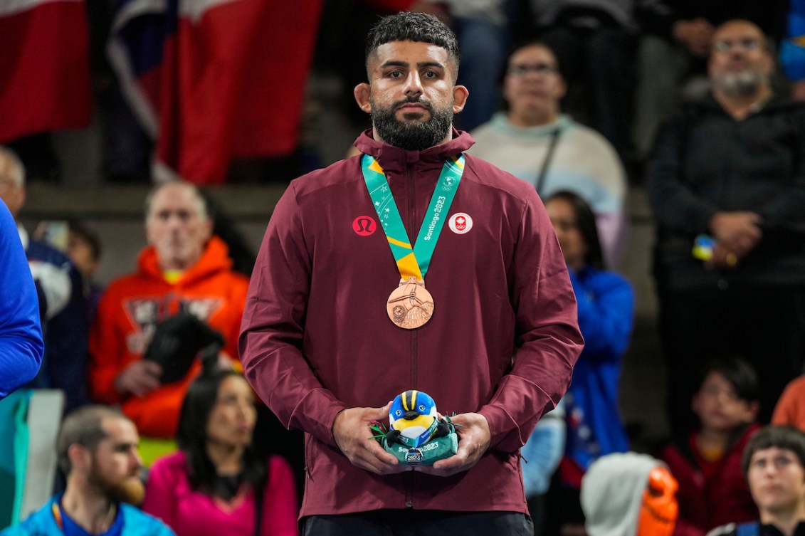 Nishan Randhawa stands on the podium wearing his bronze medal