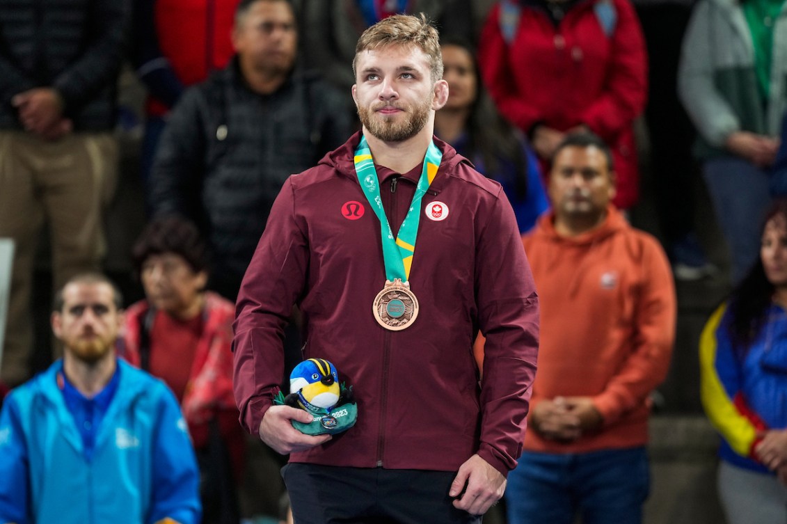 Adam Thomson stands on the podium wearing his bronze medal