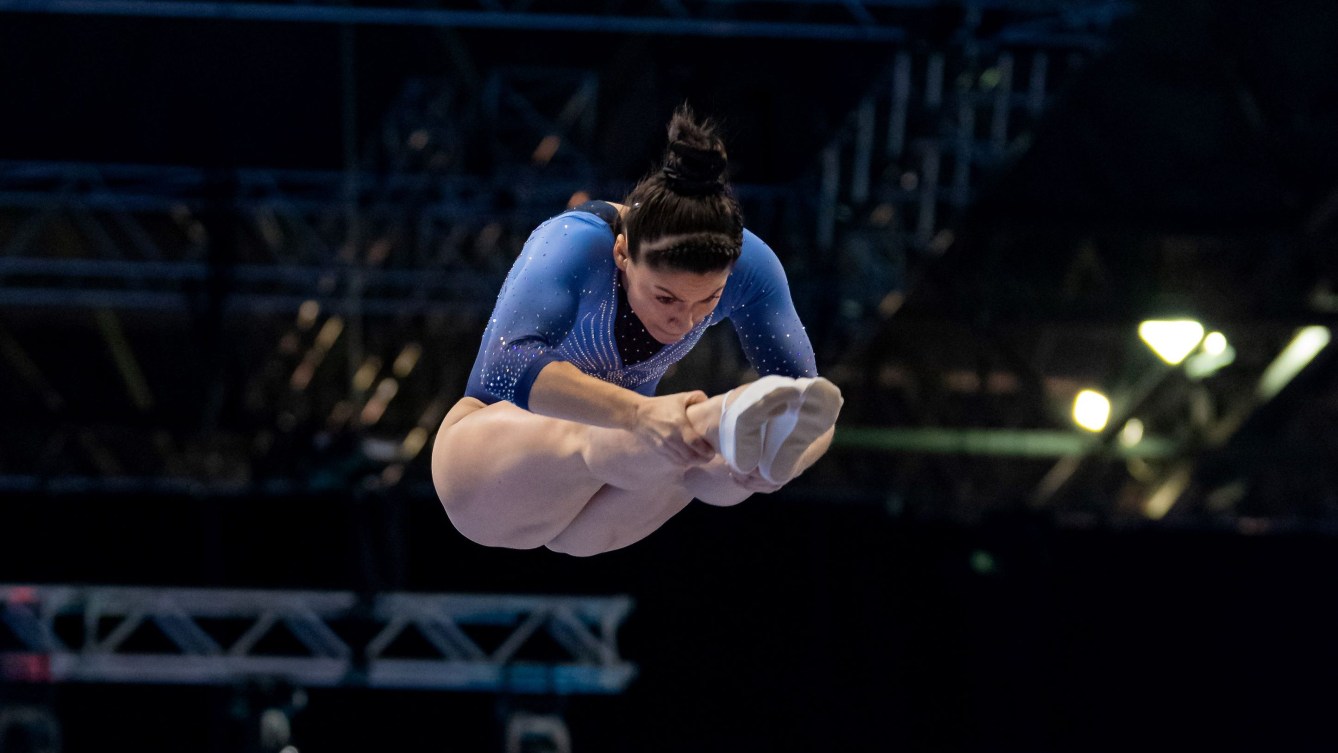 Sophiane Methot in a blue leotard performs a flip in pike position in the air