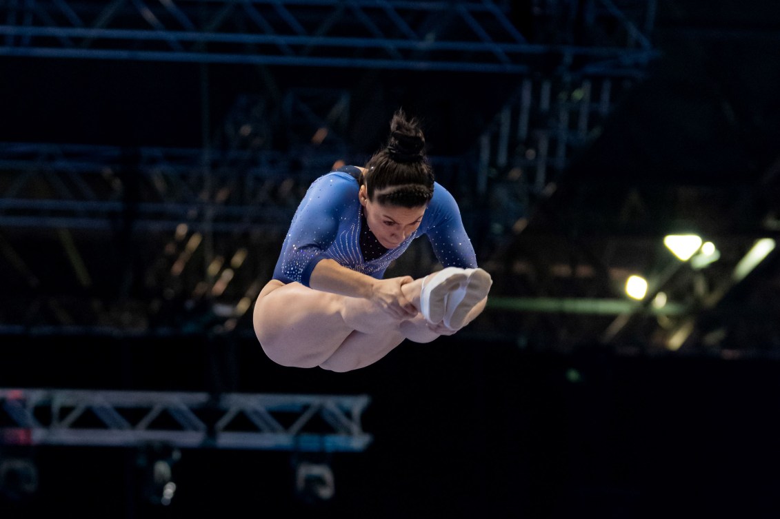Sophiane Methot in a blue leotard performs a flip in pike position in the air 