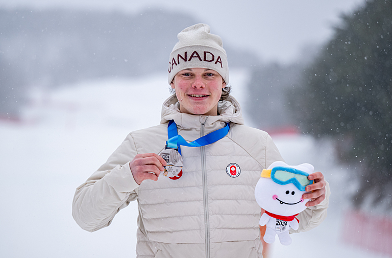 Anthony Shelly holds up his silver medal and the Gangwon 2042 mascott stuffie on the podium 