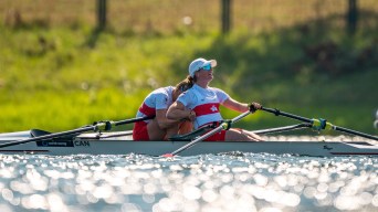 One rower leans forward to hug her teammate in front of her in the boat