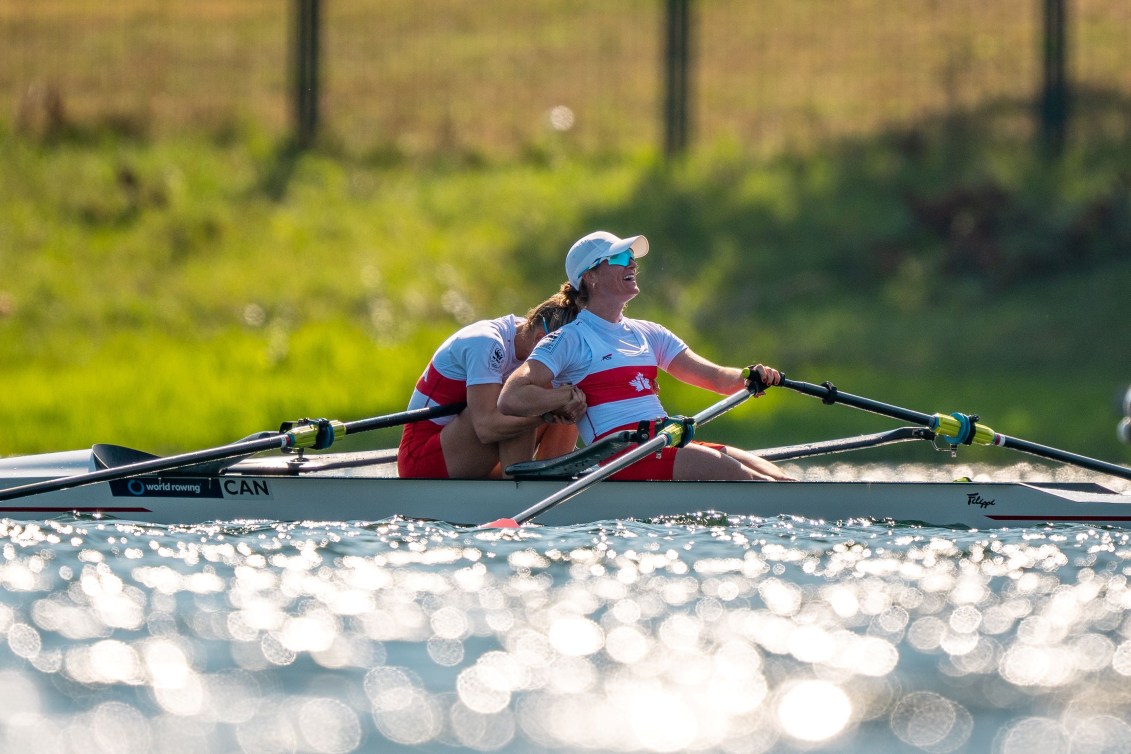 One rower leans forward to hug her teammate in front of her in the boat
