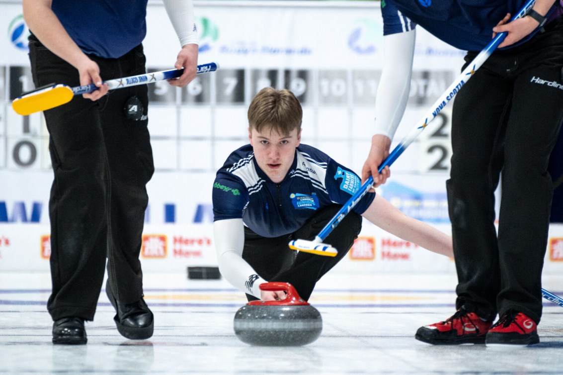 Curler in blue shirt slides to throw a red stone