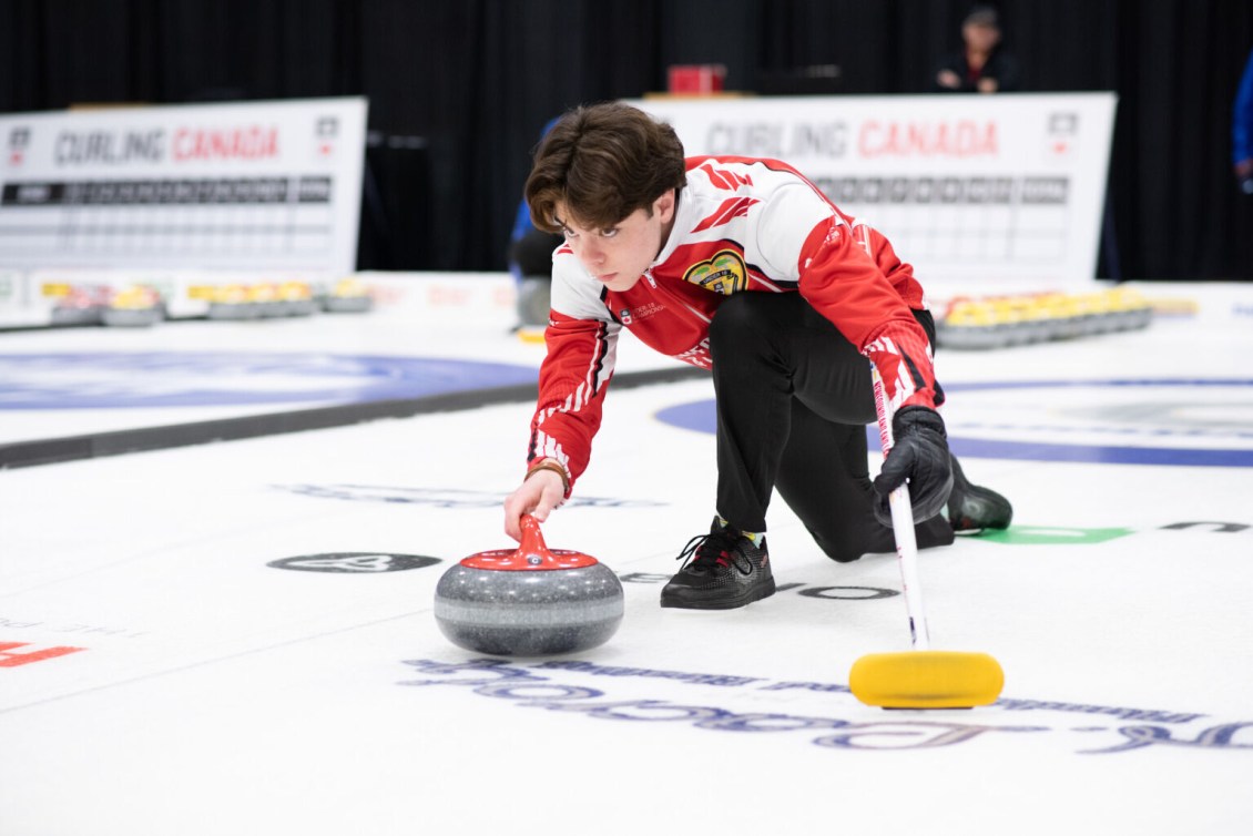 Curler in a red jacket slides to throw a red stone