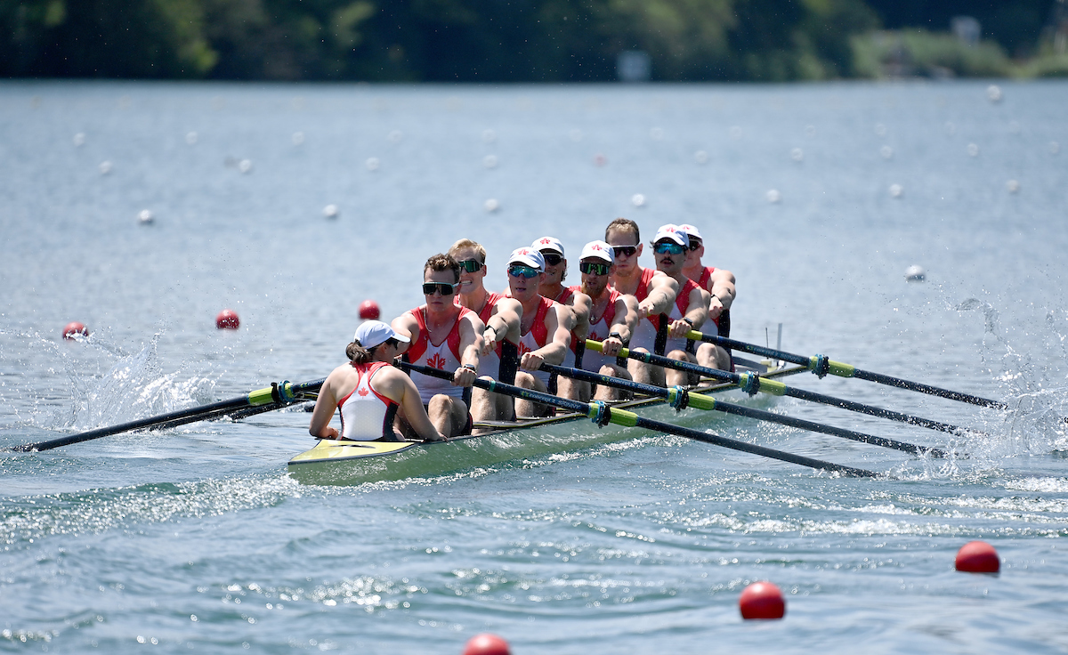 A men's eight rowing crew competes on the water with a woman coxswain