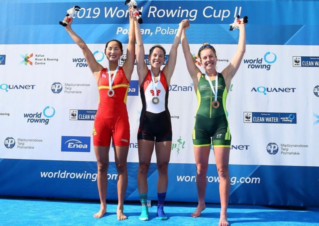 Three rowers stand together on the podium with their arms raised