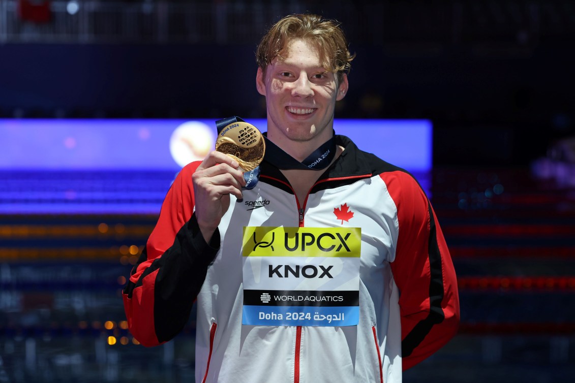 Finlay Knox holds up his gold medal while wearing a track suit jacket 