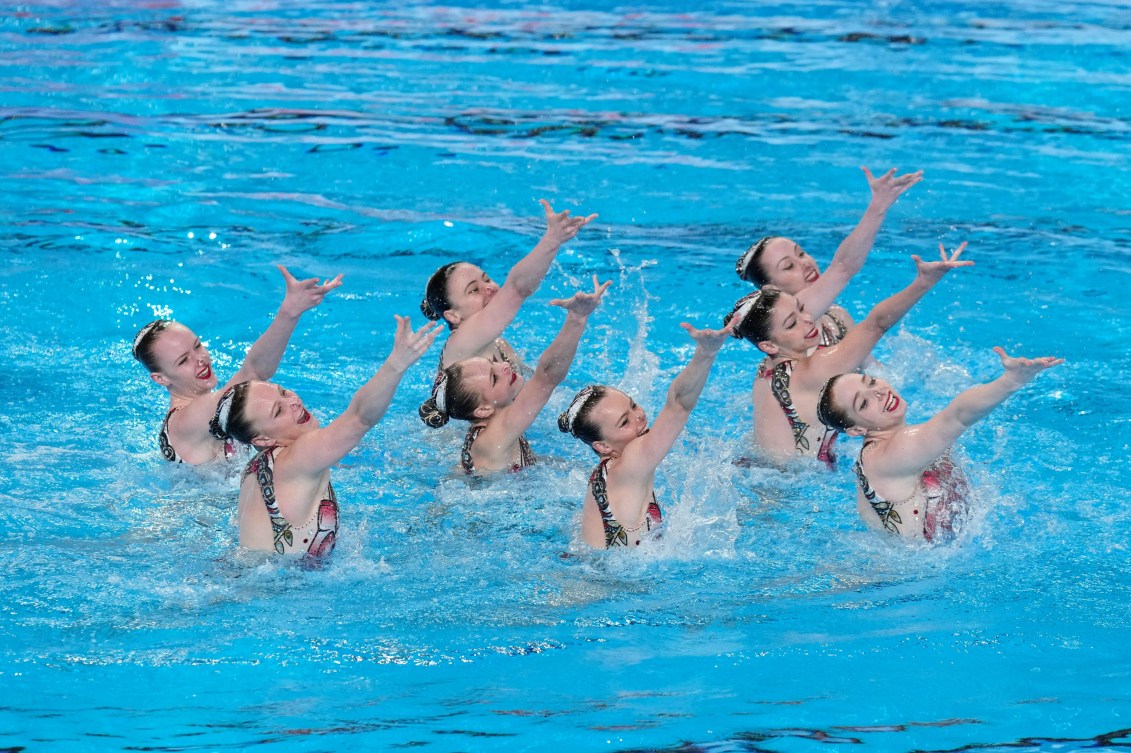 Eight artistic swimmers raise an arm in their air during their routine in the pooll 