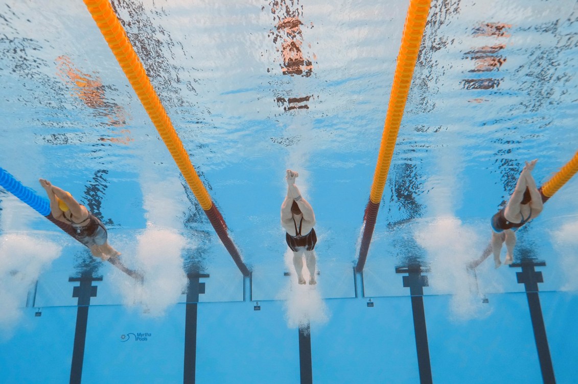 Underwater shot of three female swimmers pushing off the wall swimming backstroke 
