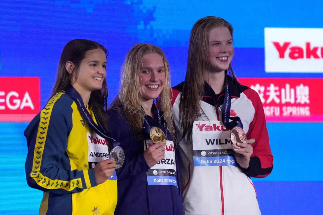 Three swimmers hold up their medals on the podium 