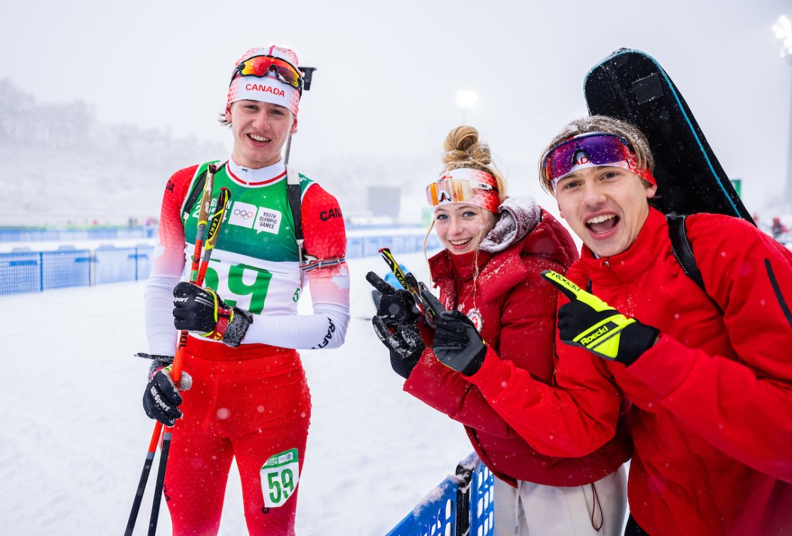 Two Canadian athletes point and smile at their biathlete teammate 