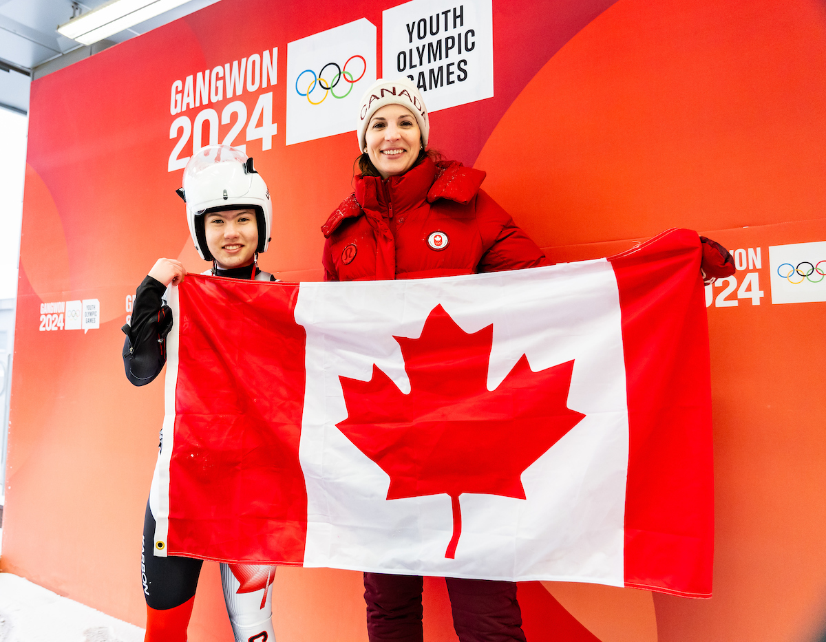 Lisa Weagle and a young luger hold the Canadian flag in the finish area of the ice track