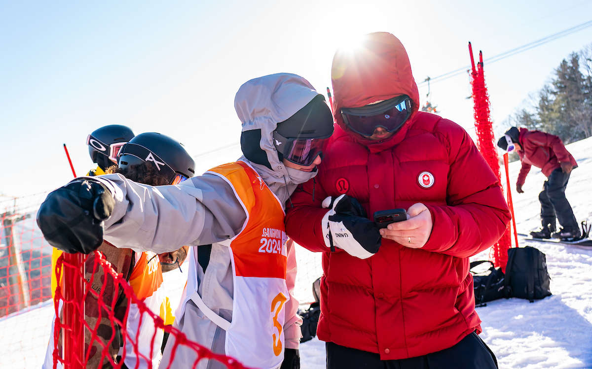 A Canadian snowboarder looks at his coach's phone screen 