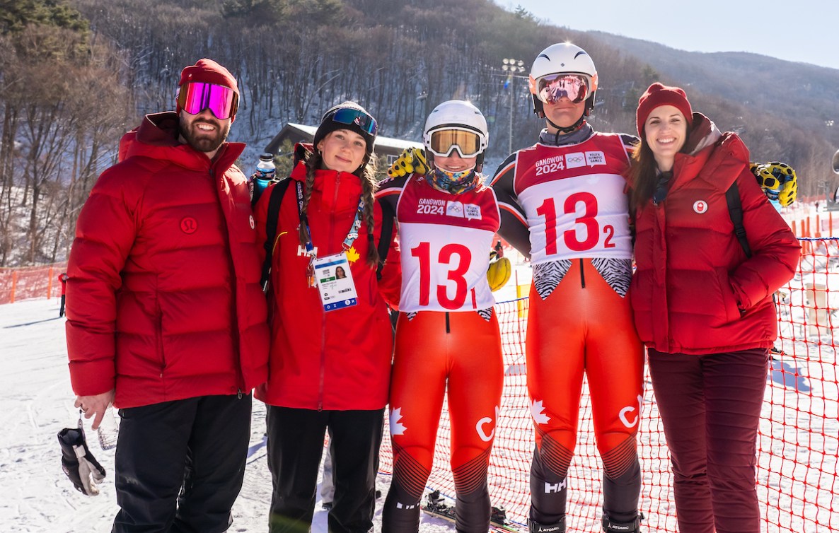 Two alpine skiers pose with their coaches and chef de mission Lisa Weagle 