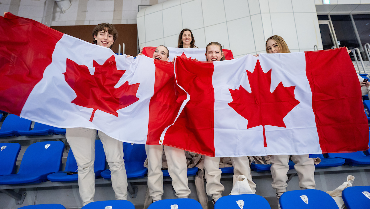 Lisa Weagle poses with Canadian figure skaters behind two big Canadian flags 