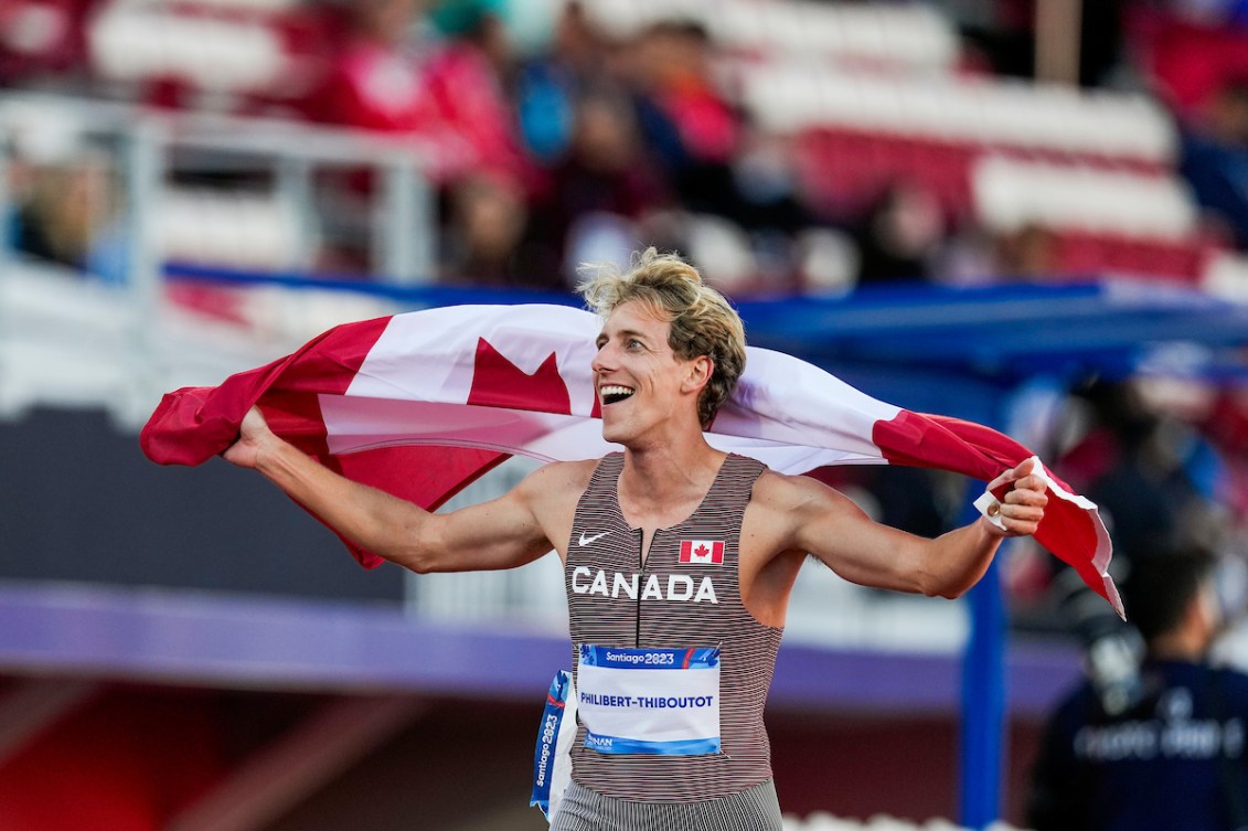 Charles Philibert-Thiboutot smiles and looks at the crowd while holding a Canadian flag above his shoulders.